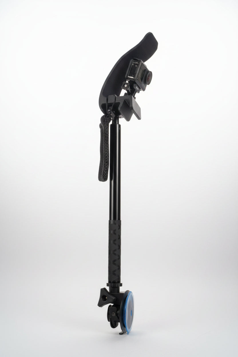 A black and gray camera rig with a suction cup, mounting bracket, and textured handle grip, photographed on a gray fabric background.